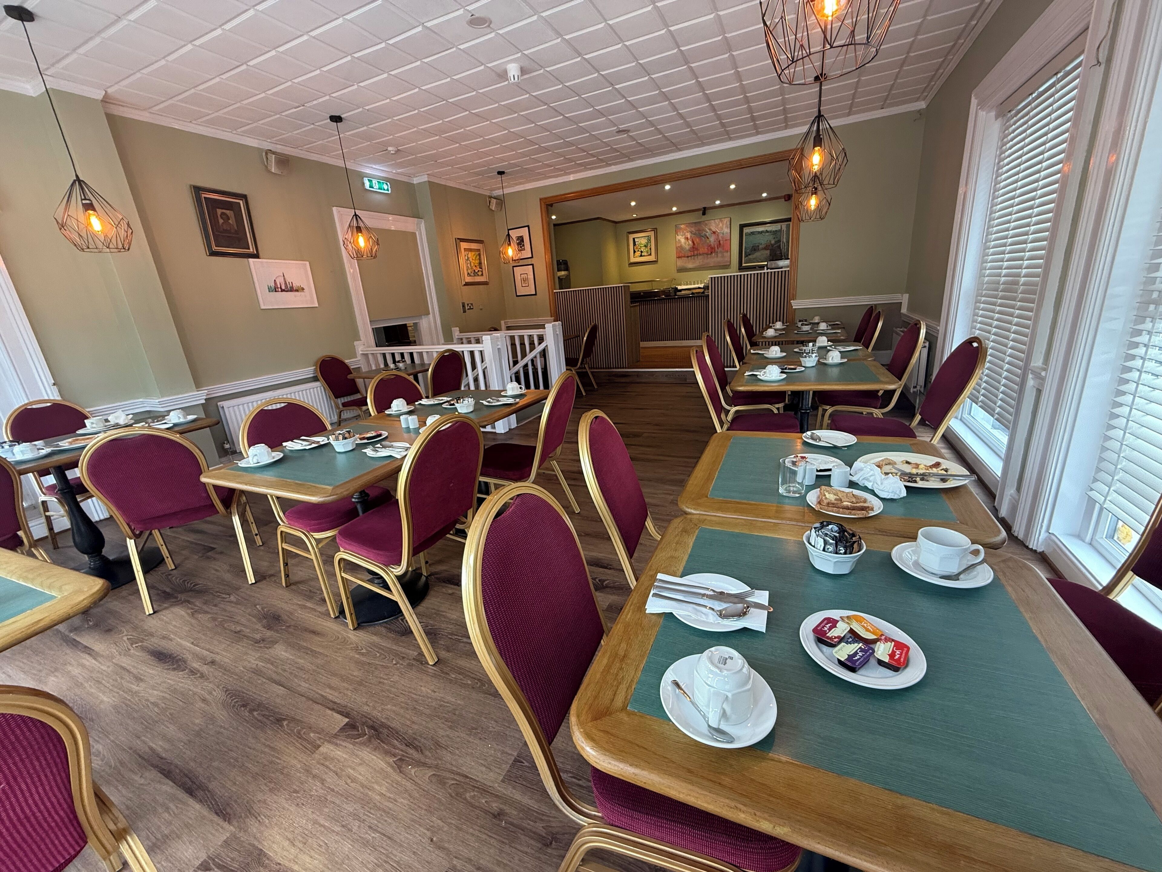 Un restaurant avec des tables en bois, des chaises à l’assise rembourrée de tissu rouge et des lampes suspendues.
