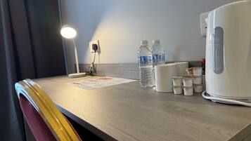 Een bureau in een hotelkamer met een lamp, twee waterflesjes, een koffiezetapparaat en verschillende kleine kopjes.