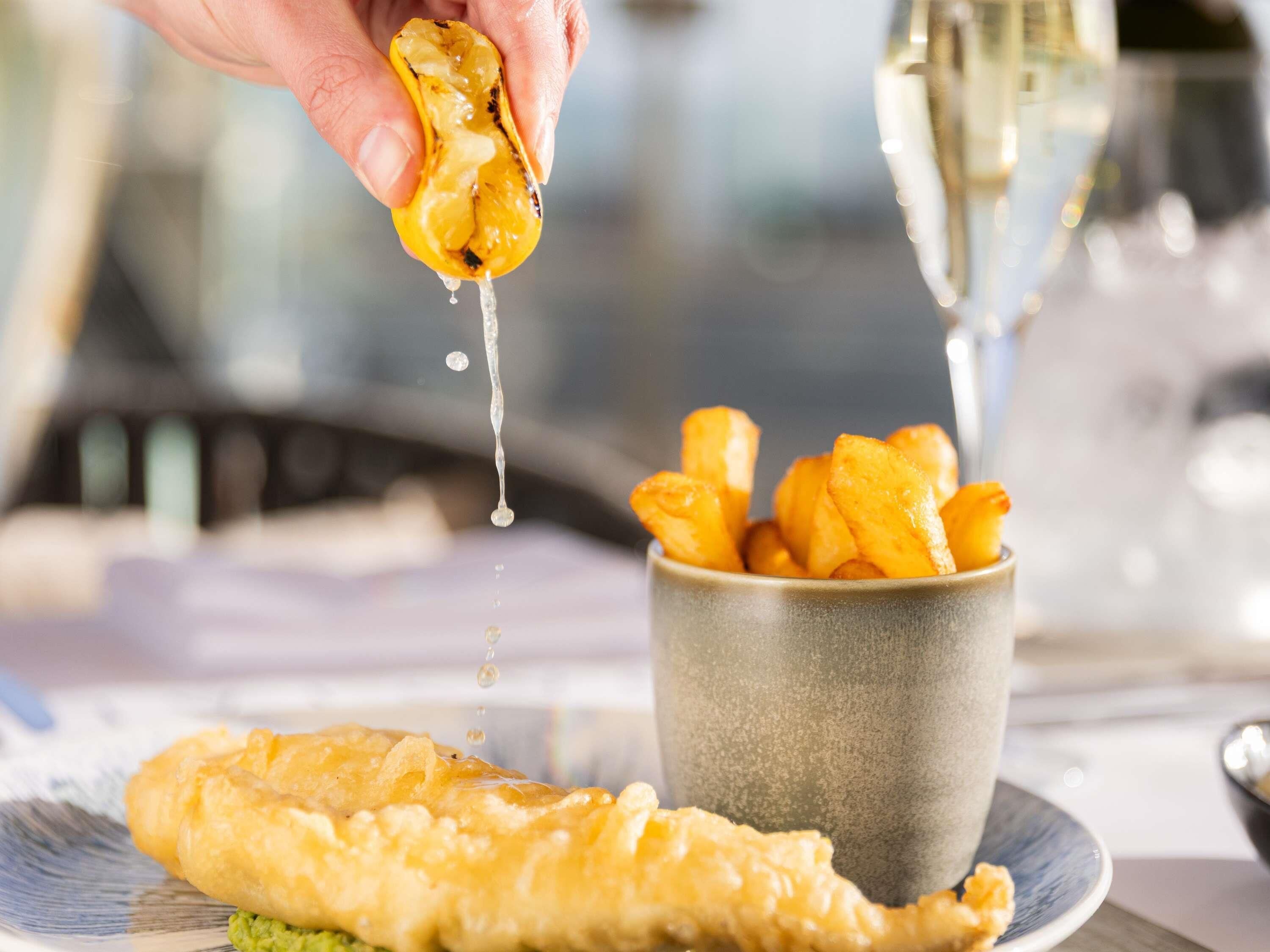 A hand holding a piece of fried food, a bowl of fries, and a plate with a breaded item.