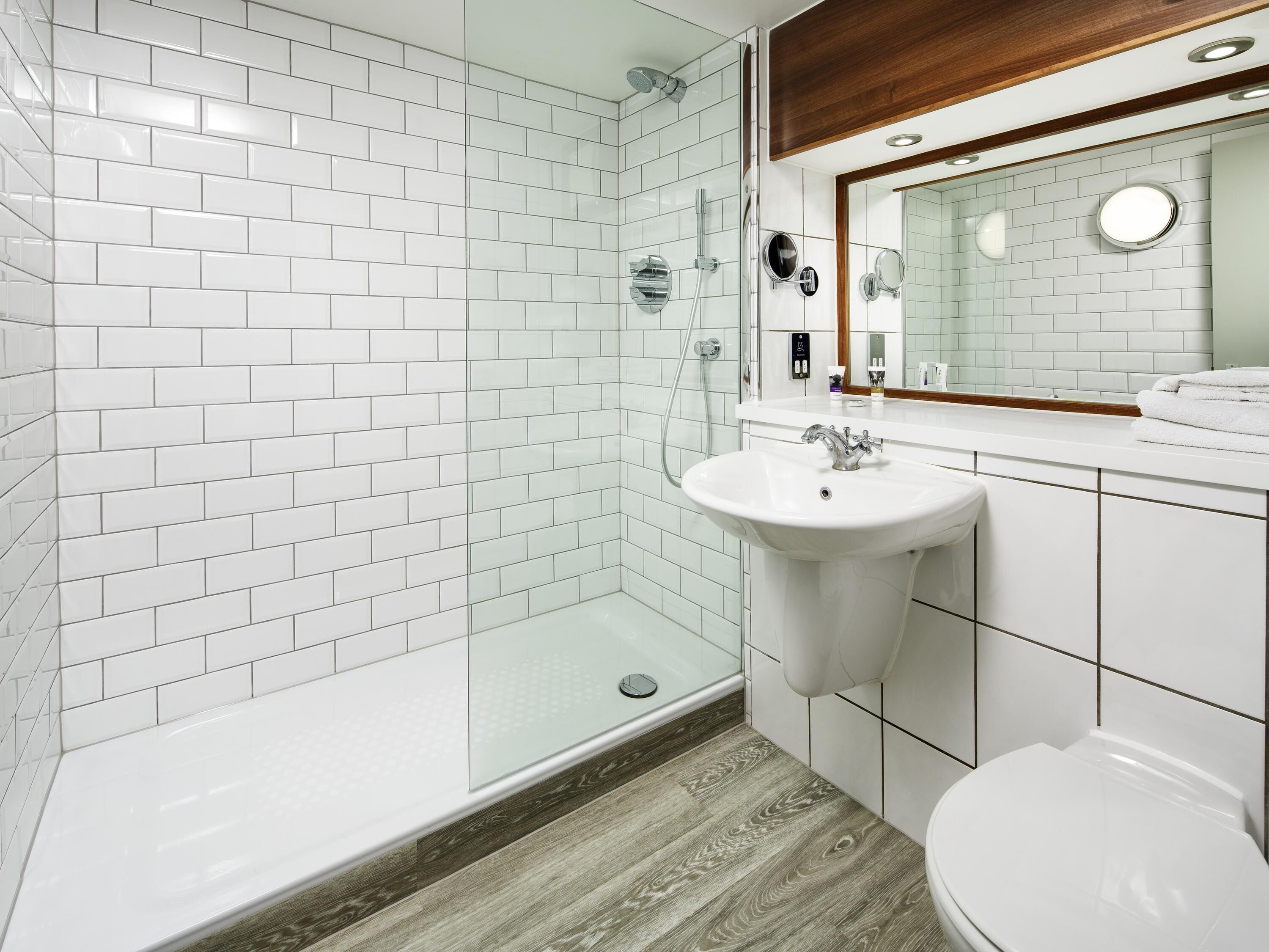 Un baño moderno con azulejos blancos tipo metro, cabina de ducha de vidrio, tocador de madera y un inodoro blanco.