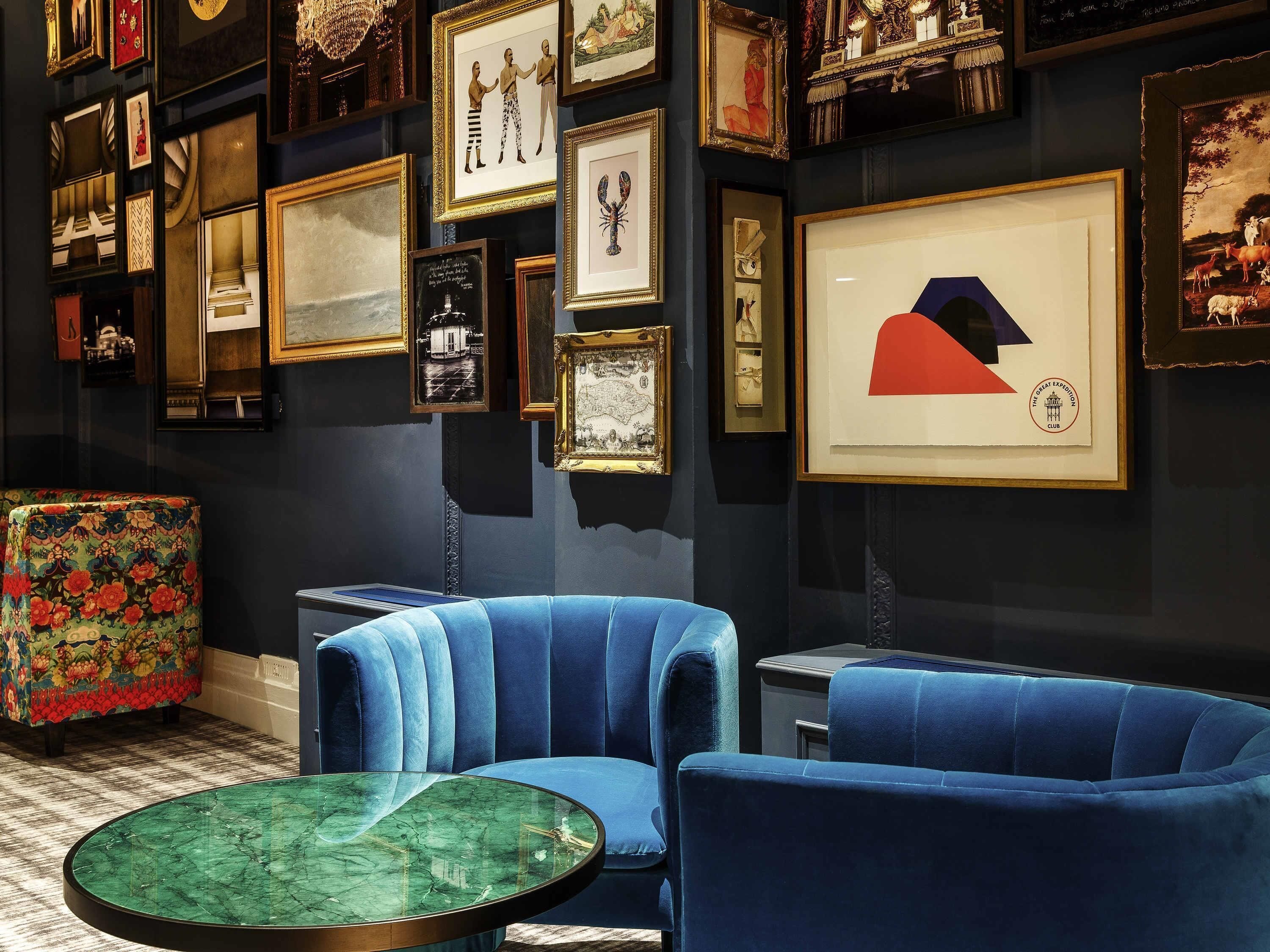 A room with a blue velvet sofa, a marble coffee table, and a wall adorned with framed artwork.