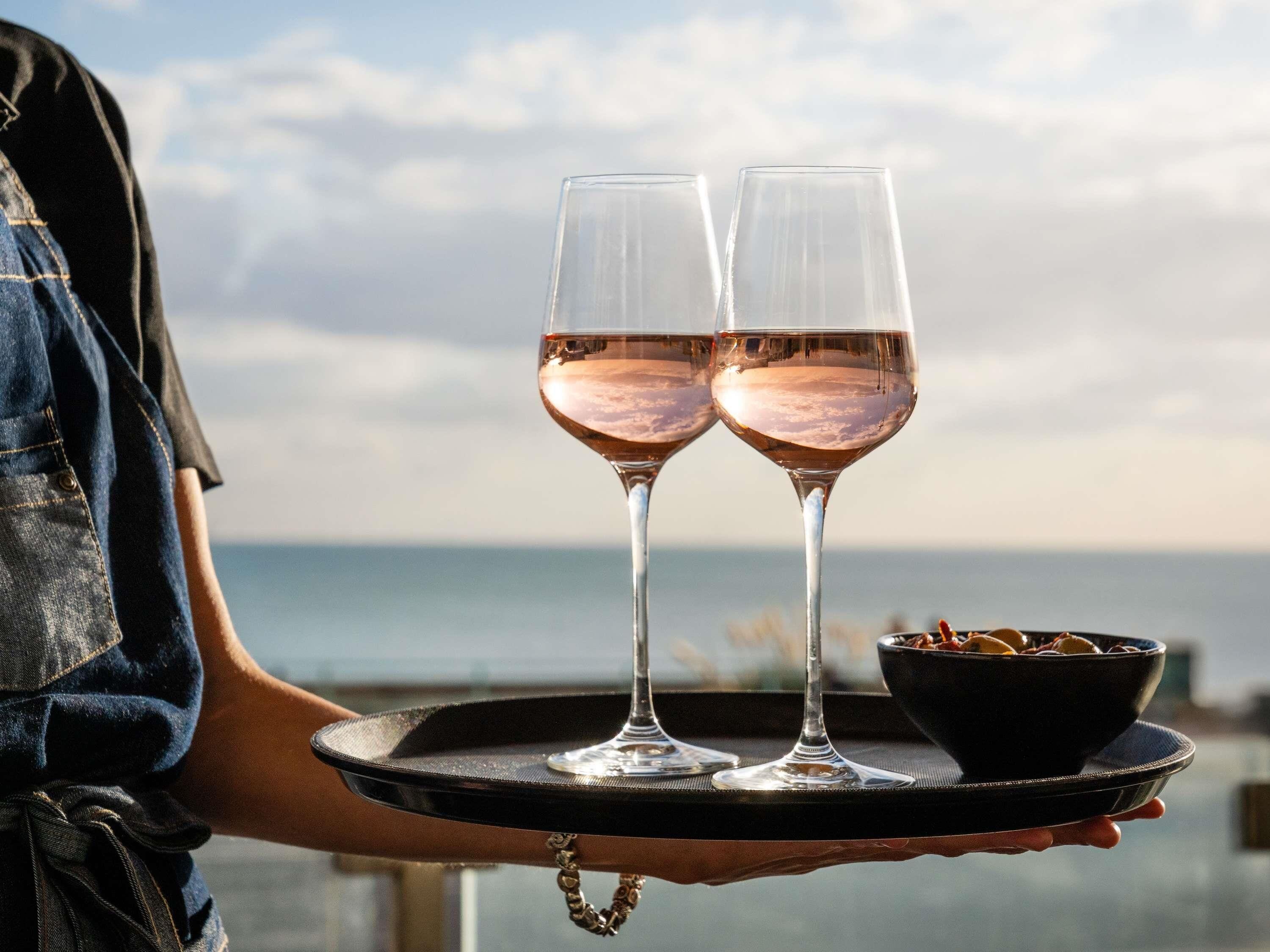 Una persona sosteniendo una bandeja con dos vasos de vino rosado y un bol de aperitivos.