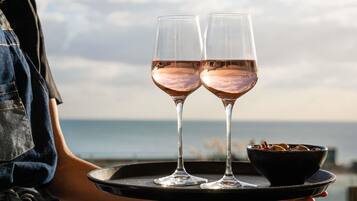 Una persona sosteniendo una bandeja con dos vasos de vino rosado y un bol de aperitivos.