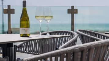 Een fles Bolney Estate Pinot Grigio wijn en twee glazen op een tafel, met rieten stoelen, met uitzicht op zee.