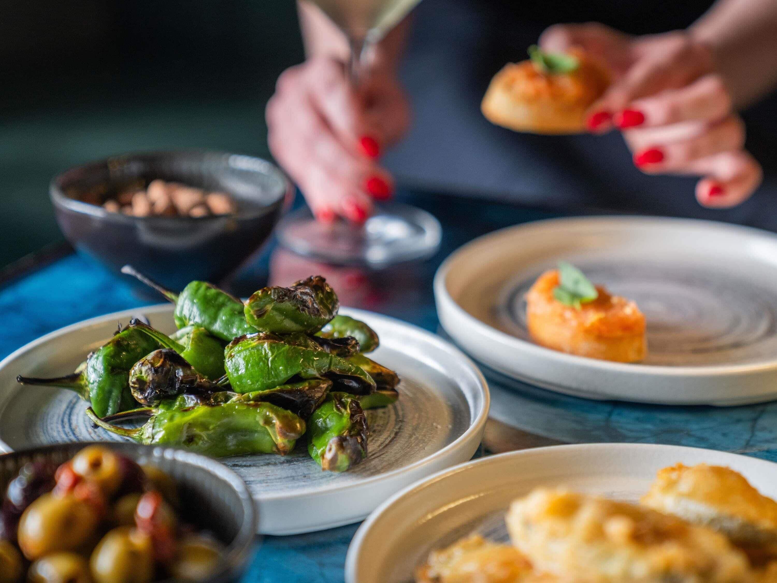Una mesa con varios platos, entre ellos pimientos asados y aceitunas.