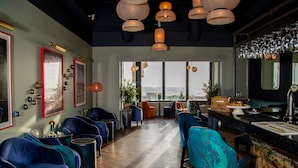 A bar area with seating, a view of the ocean, and a bar counter with a wine glass rack. - Mercure Brighton Seafront Hotel (Brighton)