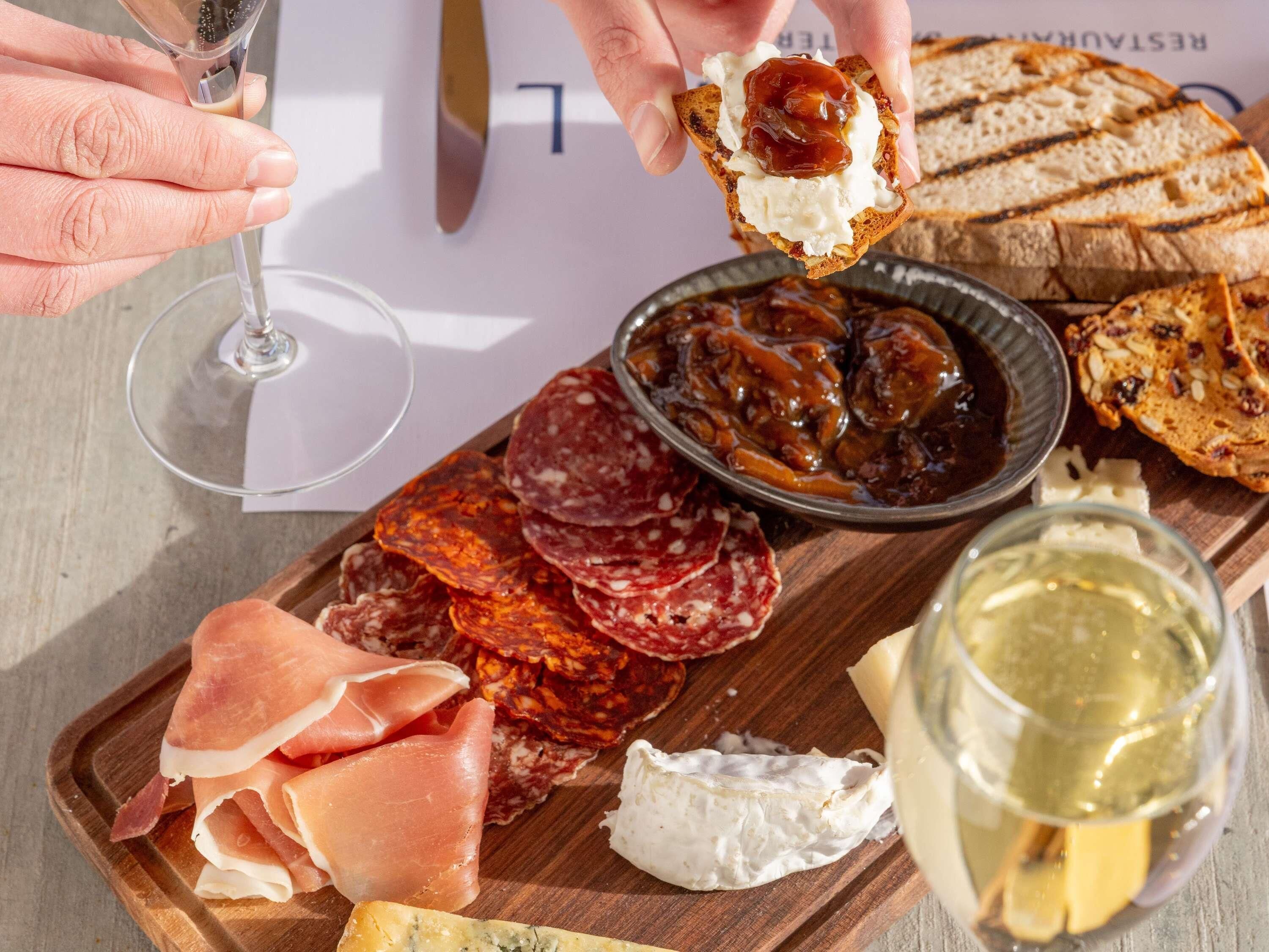 A charcuterie board with various meats, cheese, and bread, accompanied by a glass of white wine.