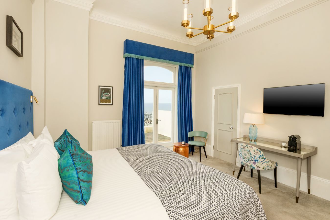A hotel room with a bed, a desk, a chair, a TV, and a balcony view.