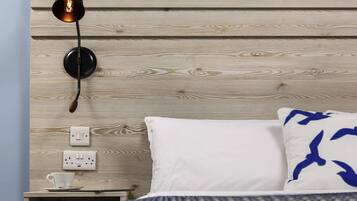 A bedroom with a wooden headboard, a bedside table with a cup and saucer, a lamp, and a bed with a patterned blanket and pillows.