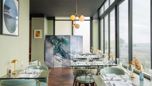 A restaurant with a view of the sea, tables set with glasses and cutlery, and a large wave painting on the wall. - Mercure Brighton Seafront Hotel (Brighton)