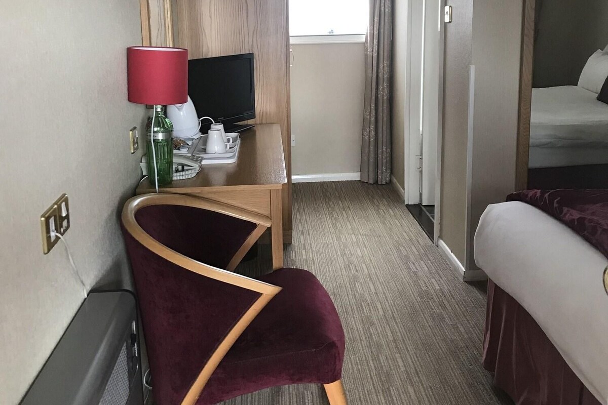 Habitació d'hotel amb un llit, escriptori amb televisió, cadira i finestra amb cortines.
