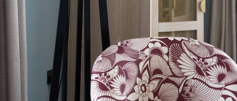A room with a wooden floor, a white lamp, a wooden cabinet with glass doors, and a floral-patterned chair.