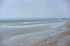 A beach with a long stretch of sand, a calm sea, and a distant shoreline with buildings.