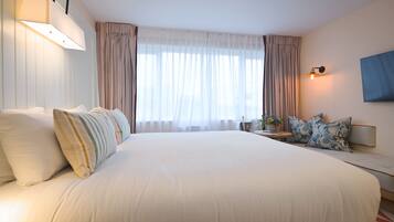 Una habitación de hotel con una cama grande, una mesita de noche con lámpara, una pequeña mesa con flores y un televisor montado en la pared.