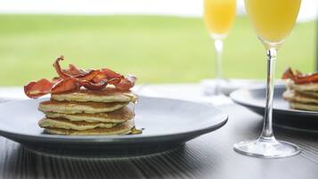 Una pila de panqueques con tocino en un plato, un vaso de jugo de naranja y un fondo desenfocado.