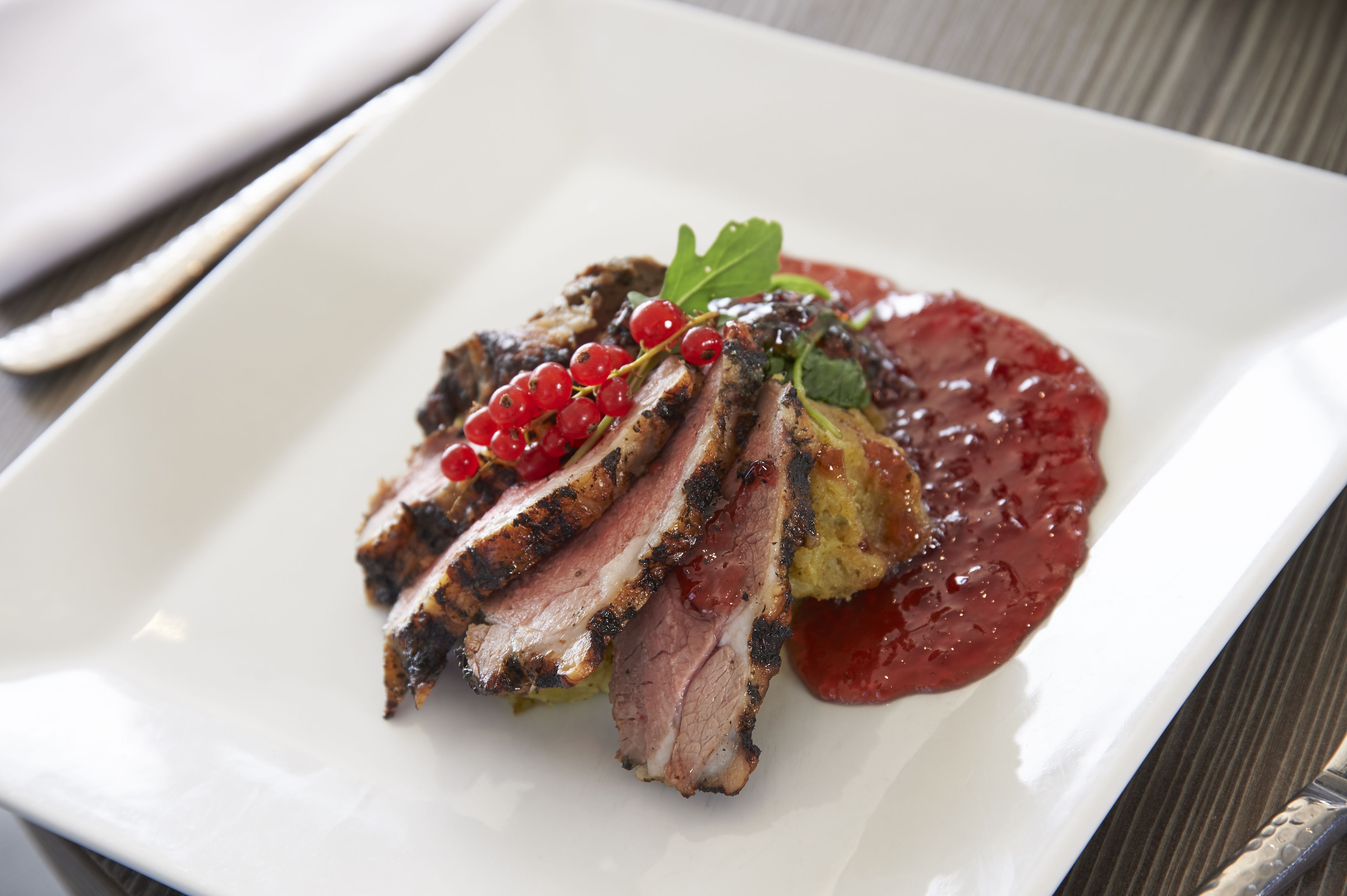 A white plate with sliced meat, red berries, and a sauce.