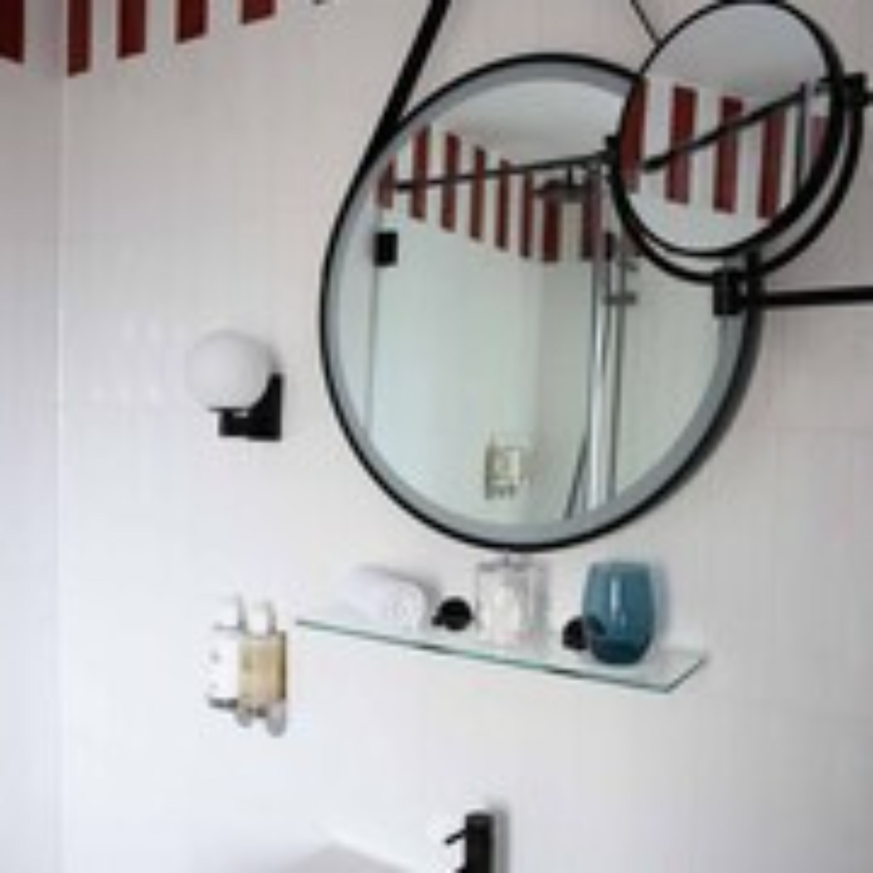 A bathroom with a round mirror, a towel rack, and a shelf with toiletries.