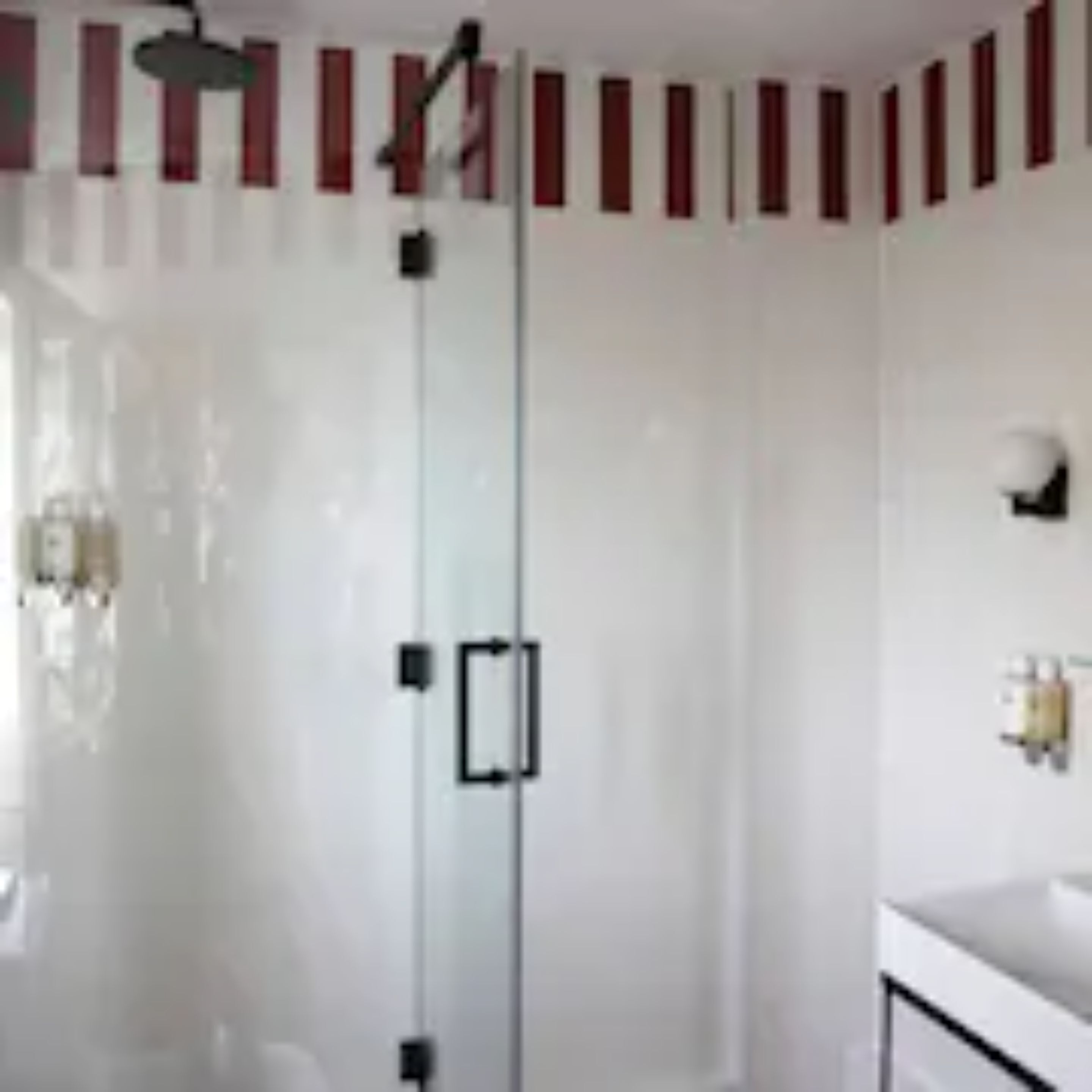 A modern bathroom with a glass shower enclosure, a white vanity with a mirror, and a wall-mounted light fixture.