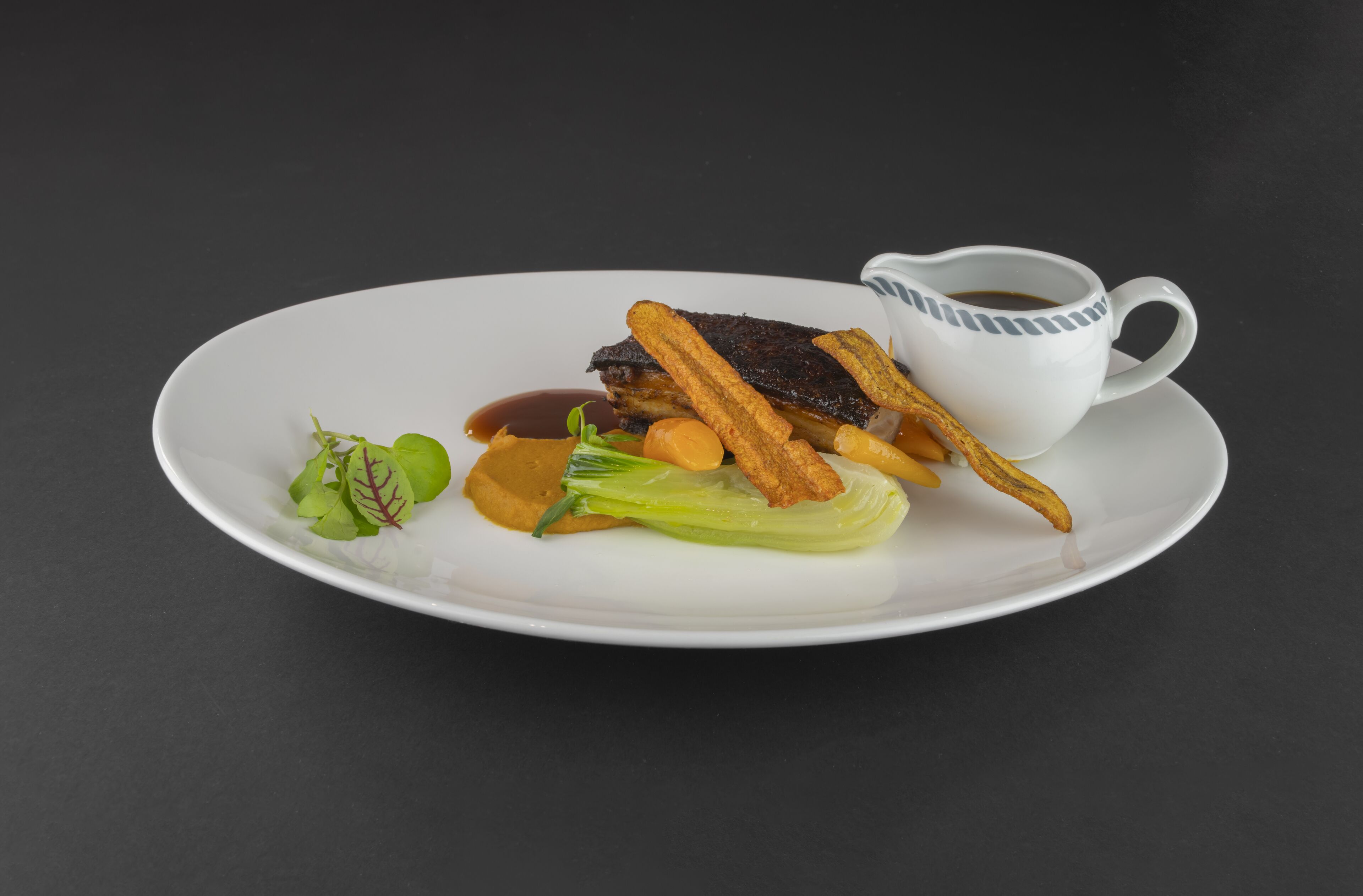 Un plato blanco con una porción de comida, que incluye un trozo de carne, verduras y una pequeña taza de salsa.