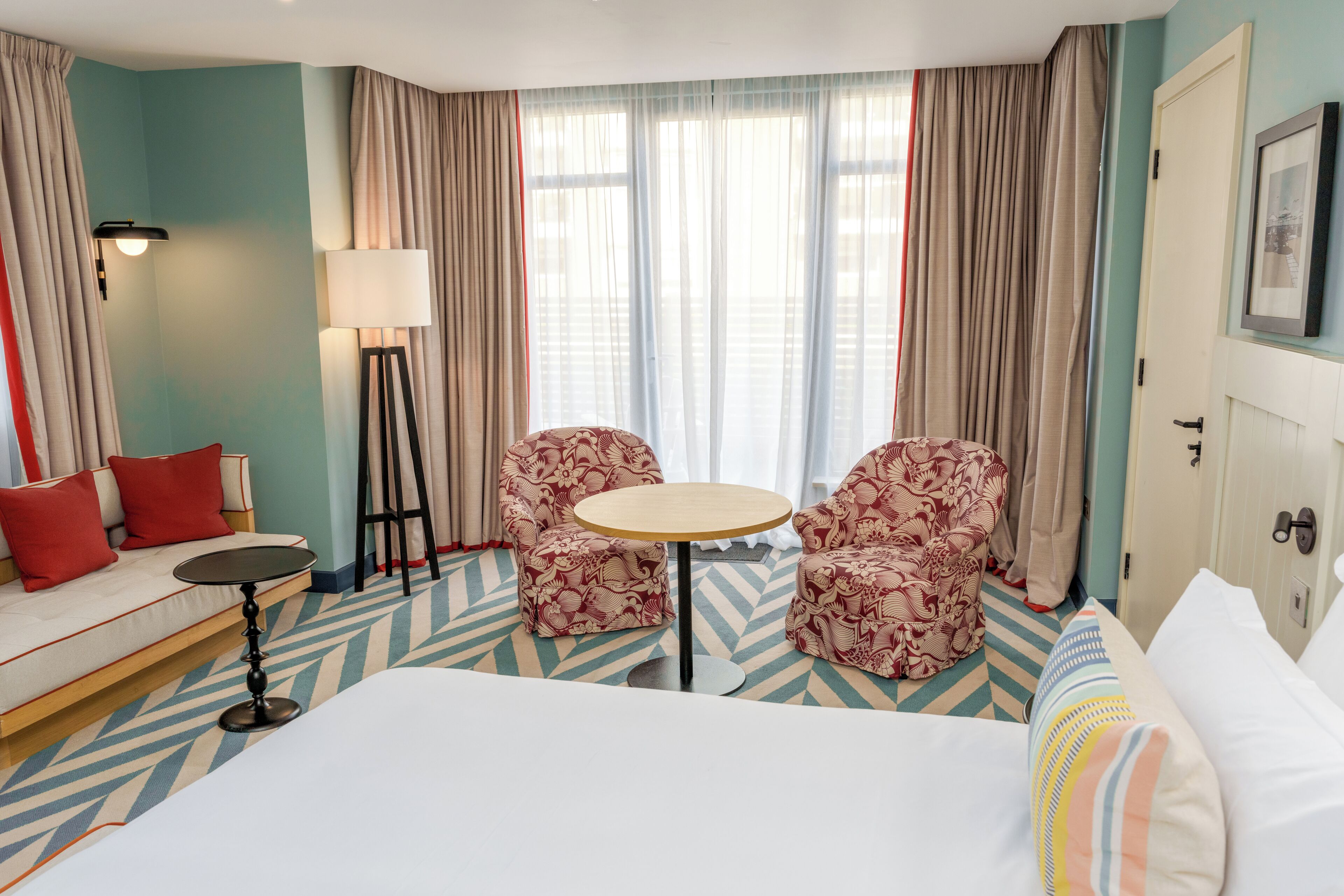 Een hotelkamer met een bed, een slaapbank, twee fauteuils, een kleine ronde tafel en een vloerlamp.