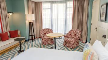 Een hotelkamer met een bed, een slaapbank, twee fauteuils, een kleine ronde tafel en een vloerlamp.