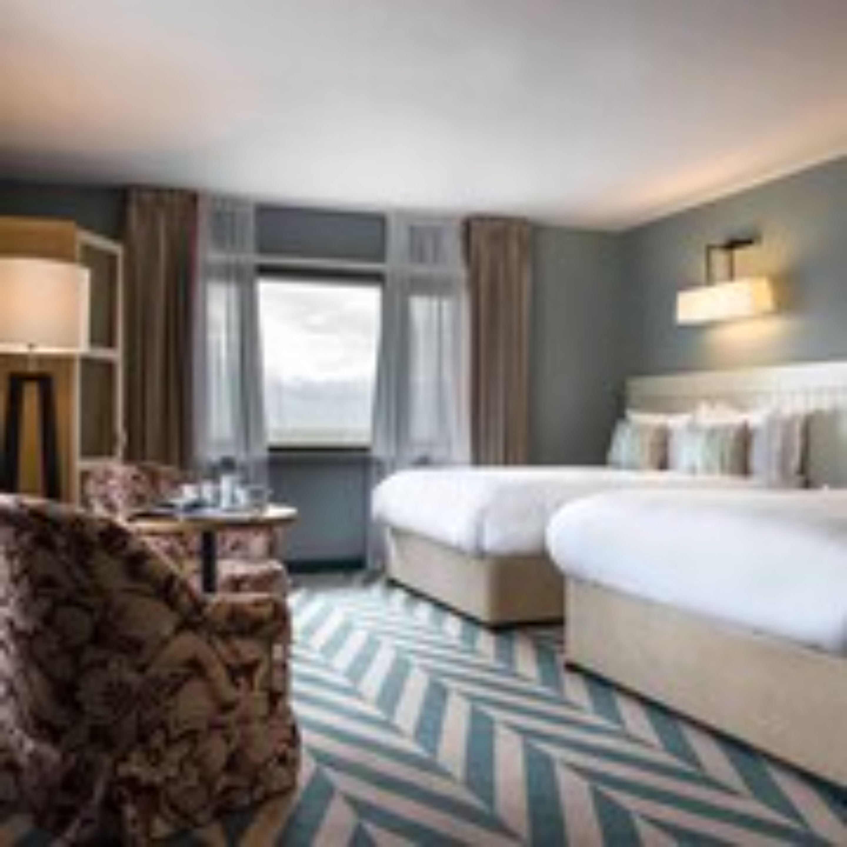 A hotel room with two beds, a desk, a chair, and a large window.