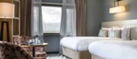 A hotel room with two beds, a desk, a chair, and a large window.