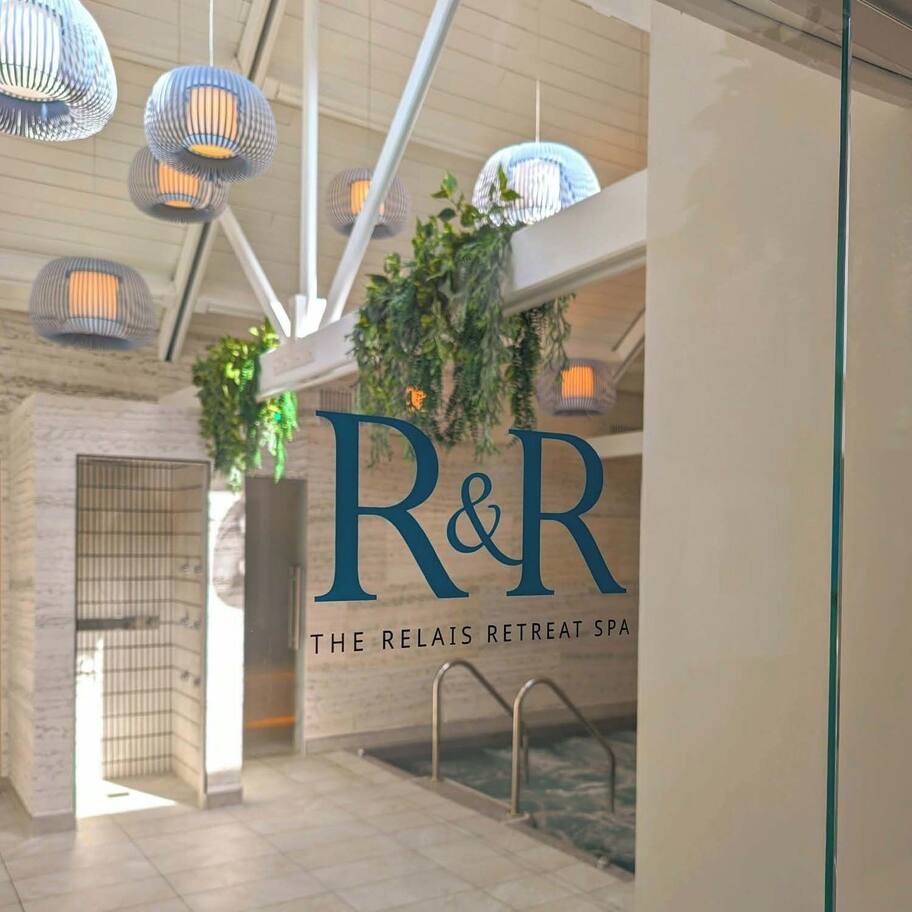 A spa interior with a large R&R logo, a pool area, and hanging pendant lights.