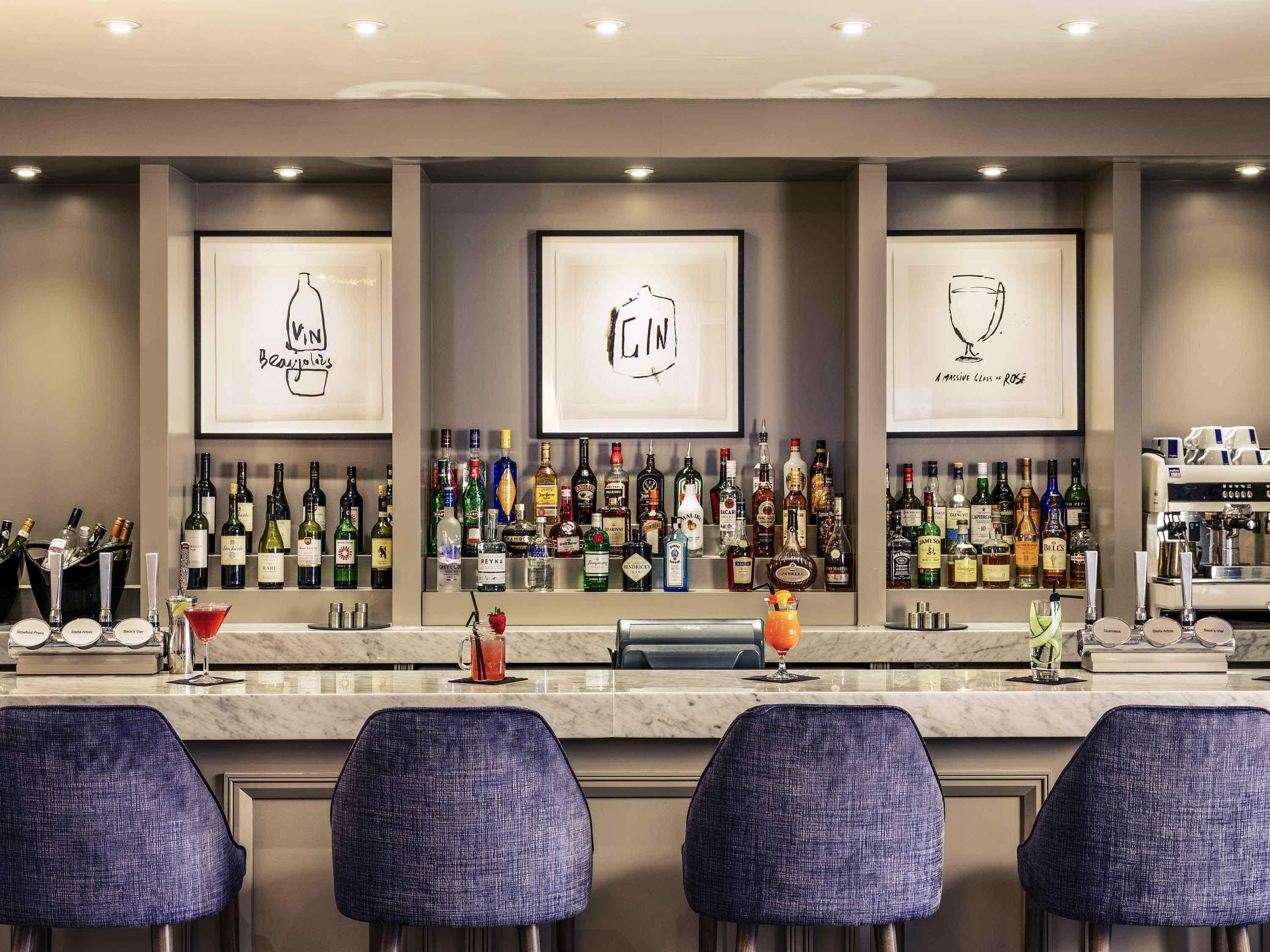Zona de bar con varias botellas de licor, obras de arte enmarcadas y taburetes.