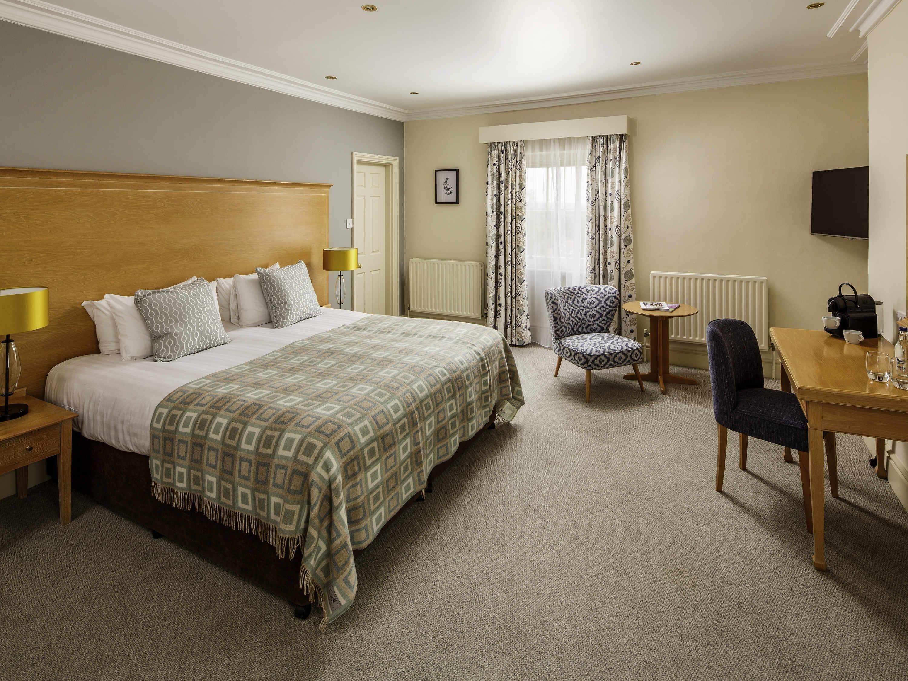 A hotel room with a large bed, a chair, a small table, a lamp, and a television.