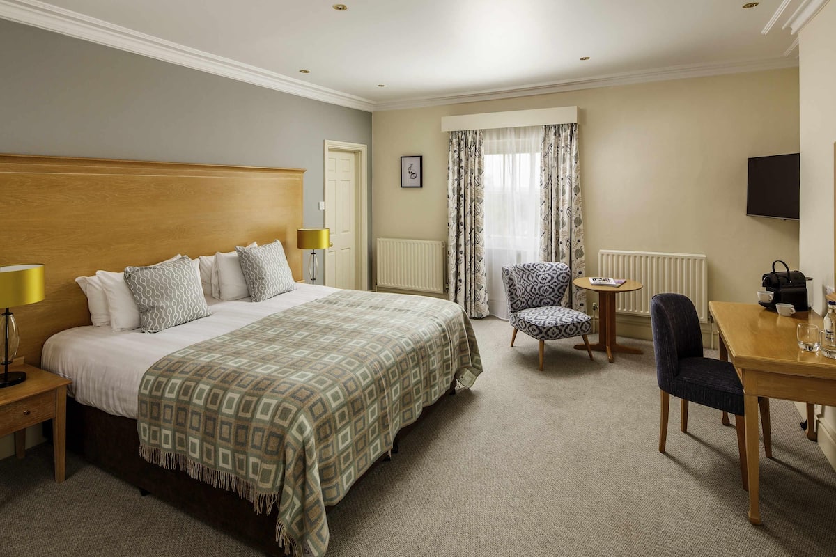 Ett hotellrum med en stor säng, en stol, ett litet bord, en lampa och en tv.