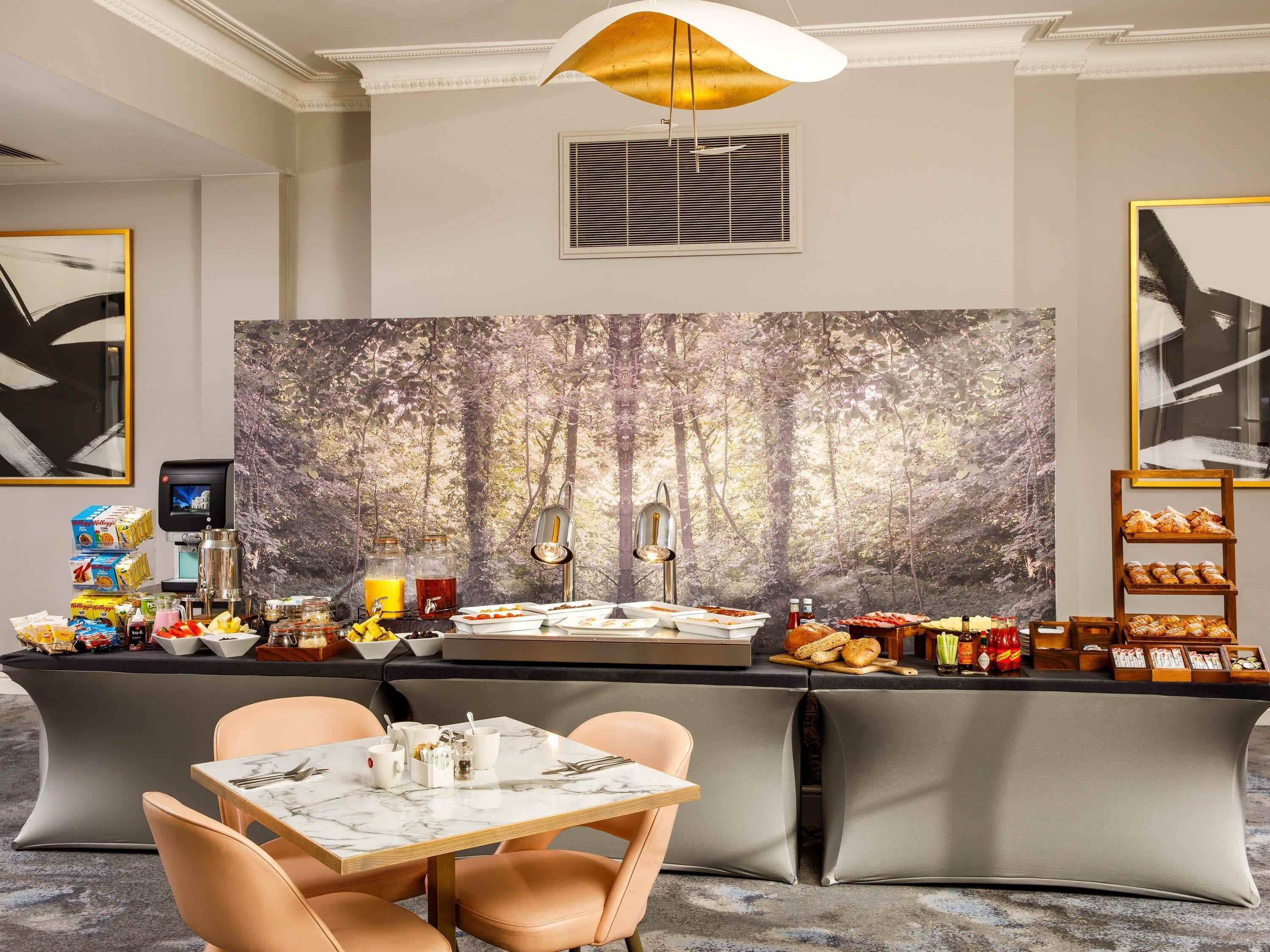 Habitación de hotel moderna con barra de desayuno, zona de estar y un mural temático de bosque.