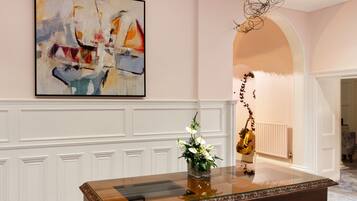 A room with a large abstract painting, a glass-top table with a vase of flowers, and a violin leaning against the wall.