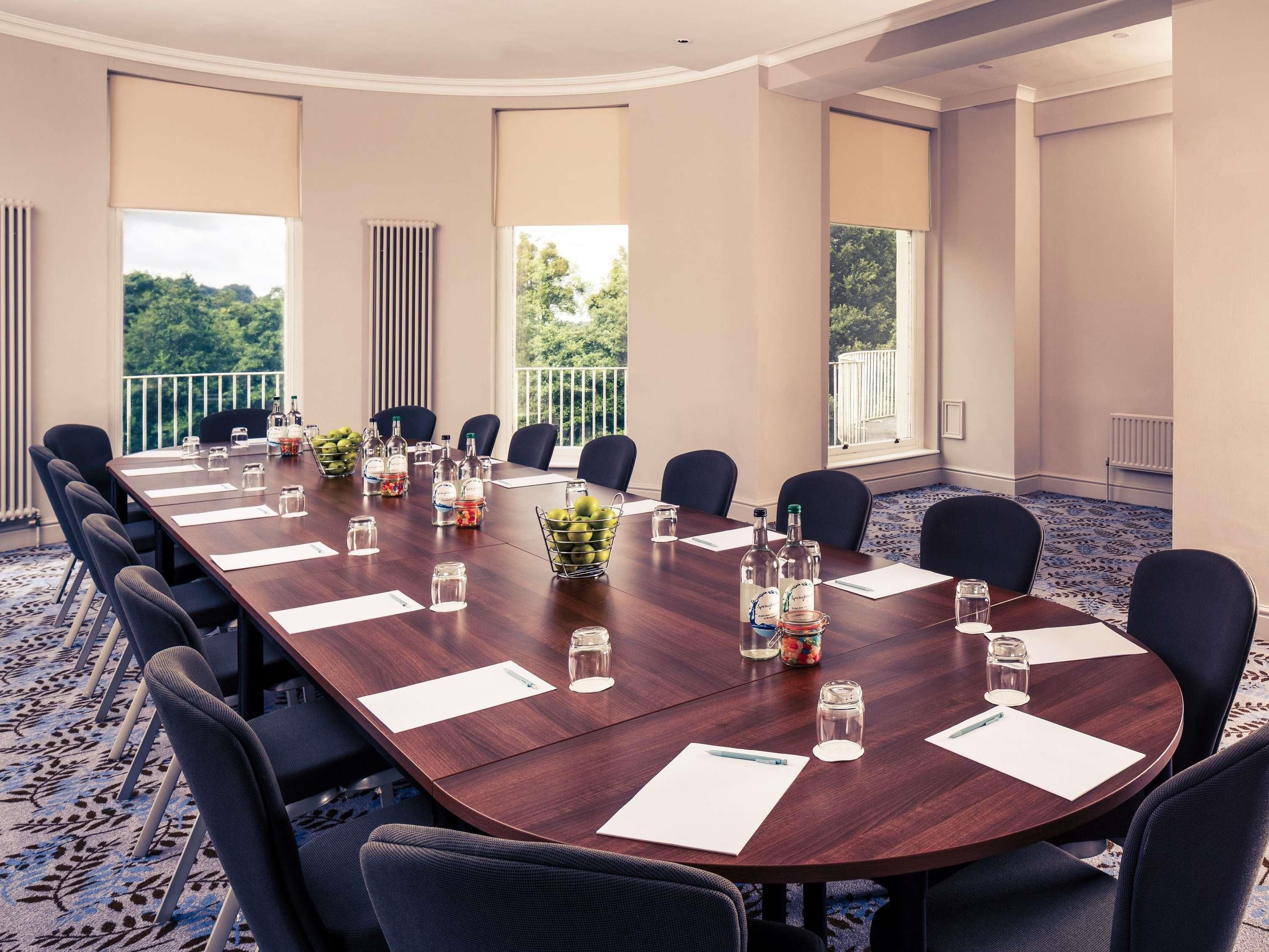 A conference room with a long table, chairs, and a view of greenery outside.