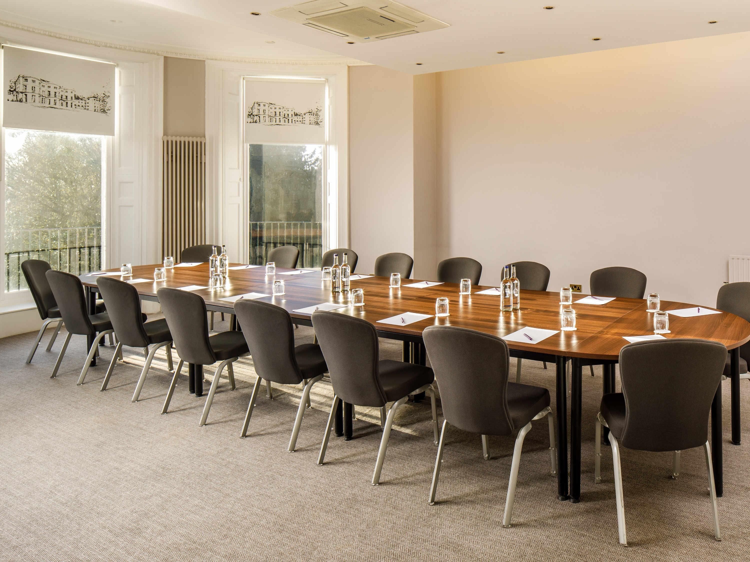 A conference room with a large wooden table, black chairs, and glass water bottles.