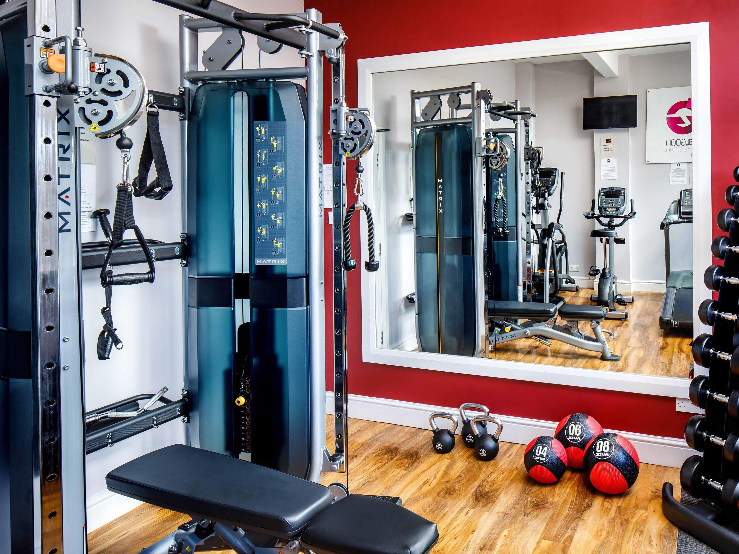 Une salle de sport équipée de miroirs, de supports pour les poids, d’un banc et de ballons d’exercice.