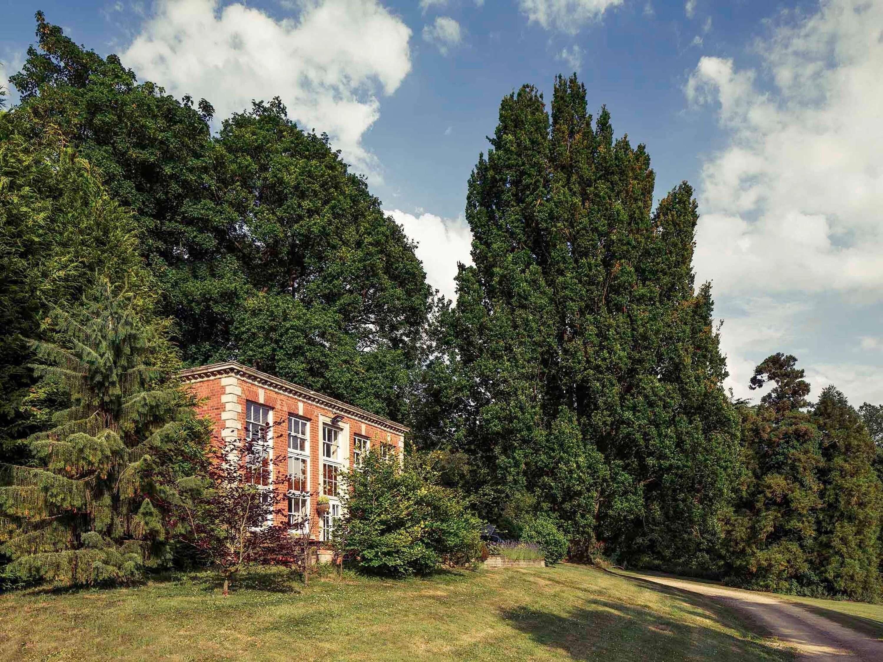 Un edificio de ladrillo con varias ventanas, rodeado de un bosque frondoso y un cielo despejado.