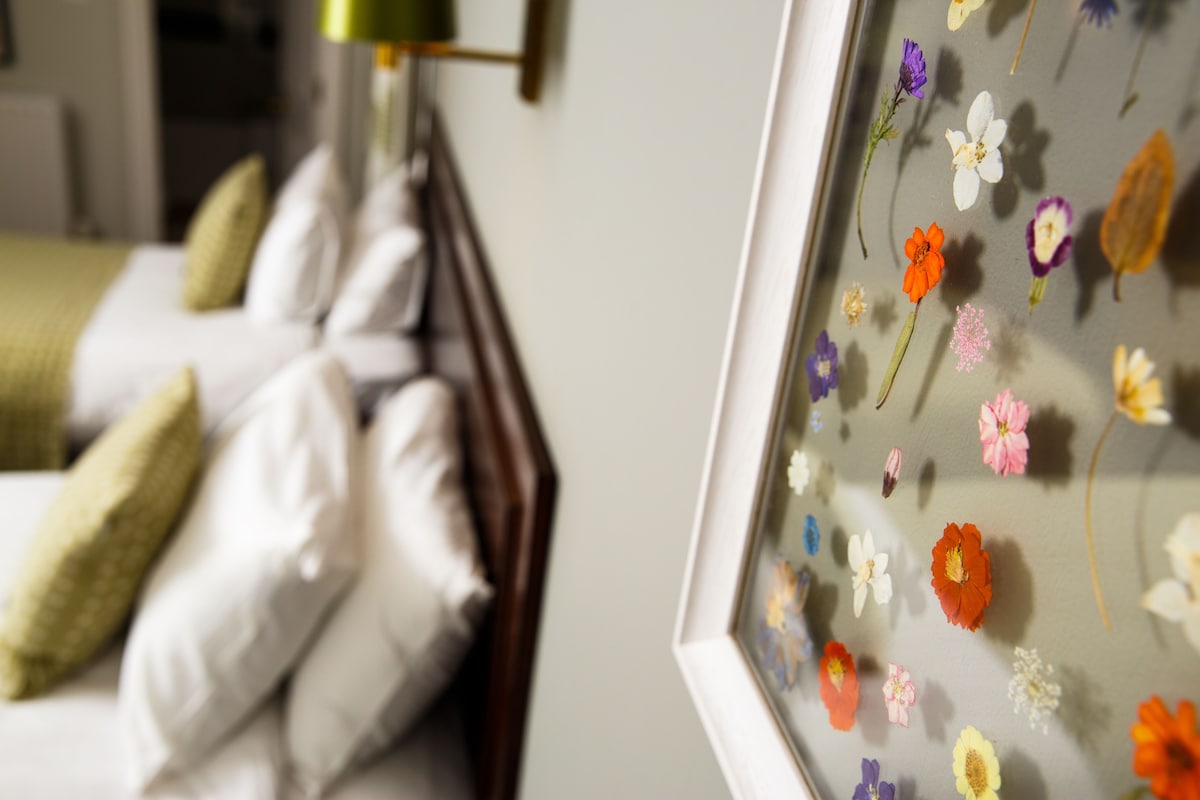 A bed with white pillows and a framed floral artwork on the wall.