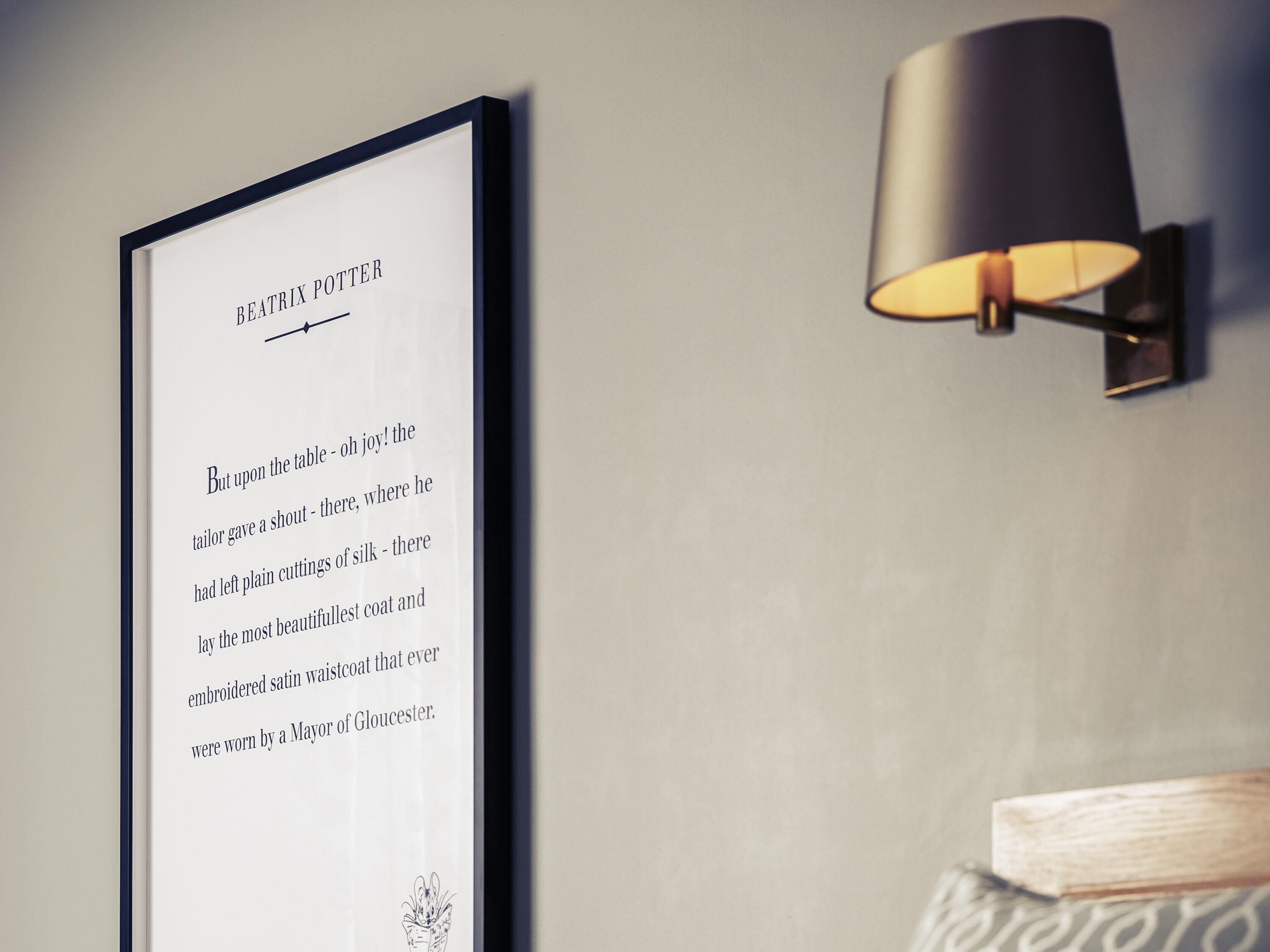 A framed text on a wall with a wall-mounted lamp beside it.