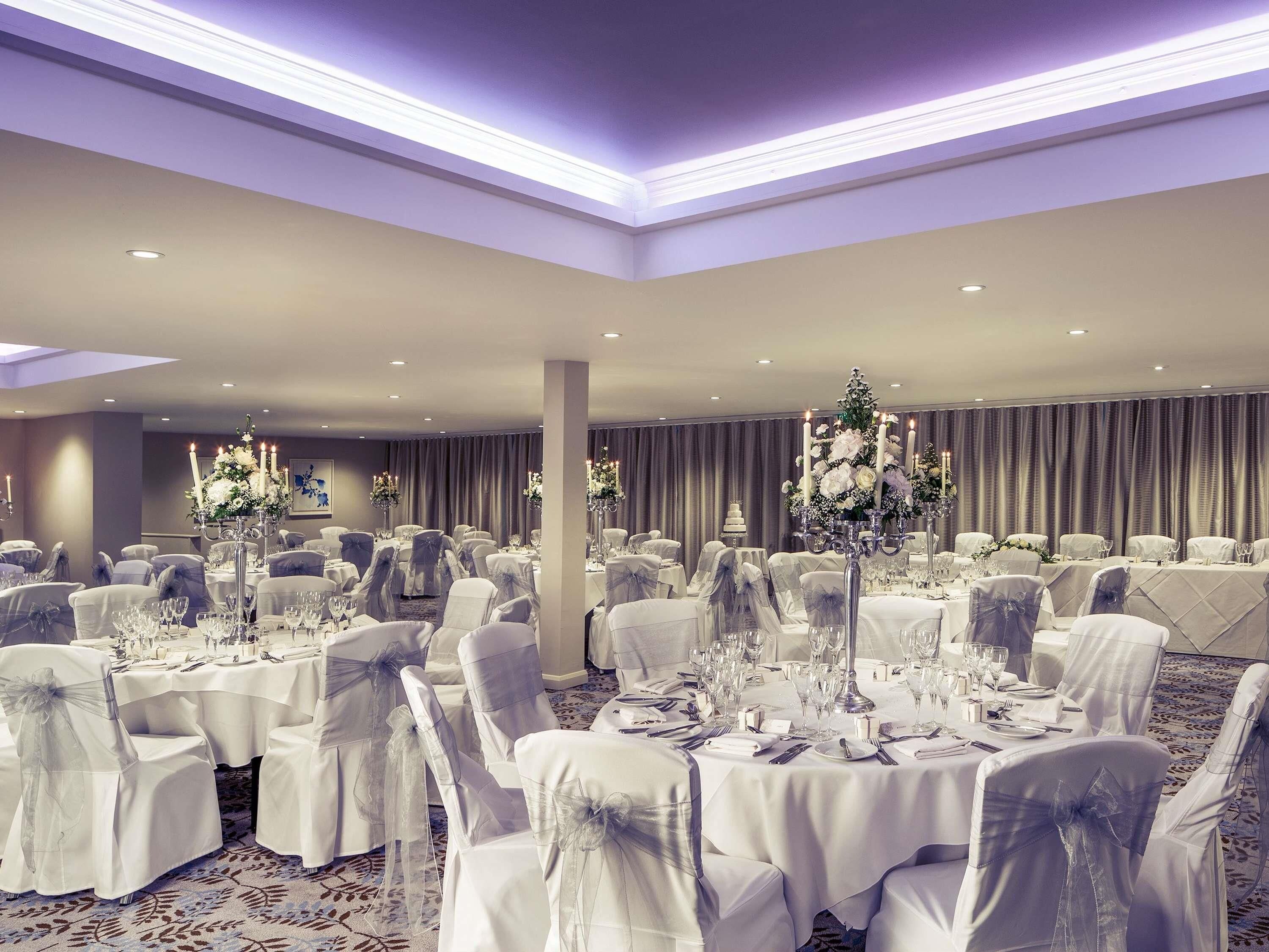 A banquet hall with round tables, chairs, and floral centerpieces.
