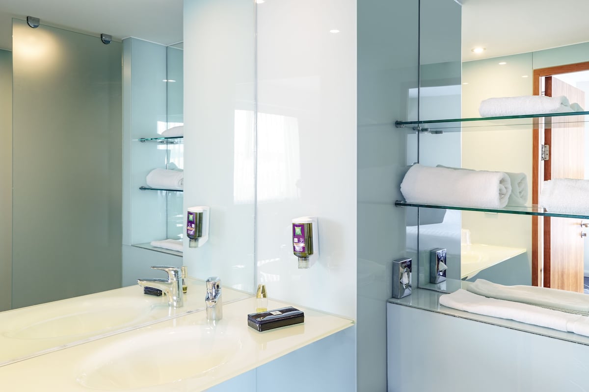 A modern bathroom with a glass shower enclosure, a large mirror, and a glass shelf with towels.