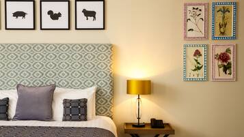 Una cama bien hecha con ropa de cama estampada, una lámpara de noche e impresiones enmarcadas de animales y plantas en la pared.