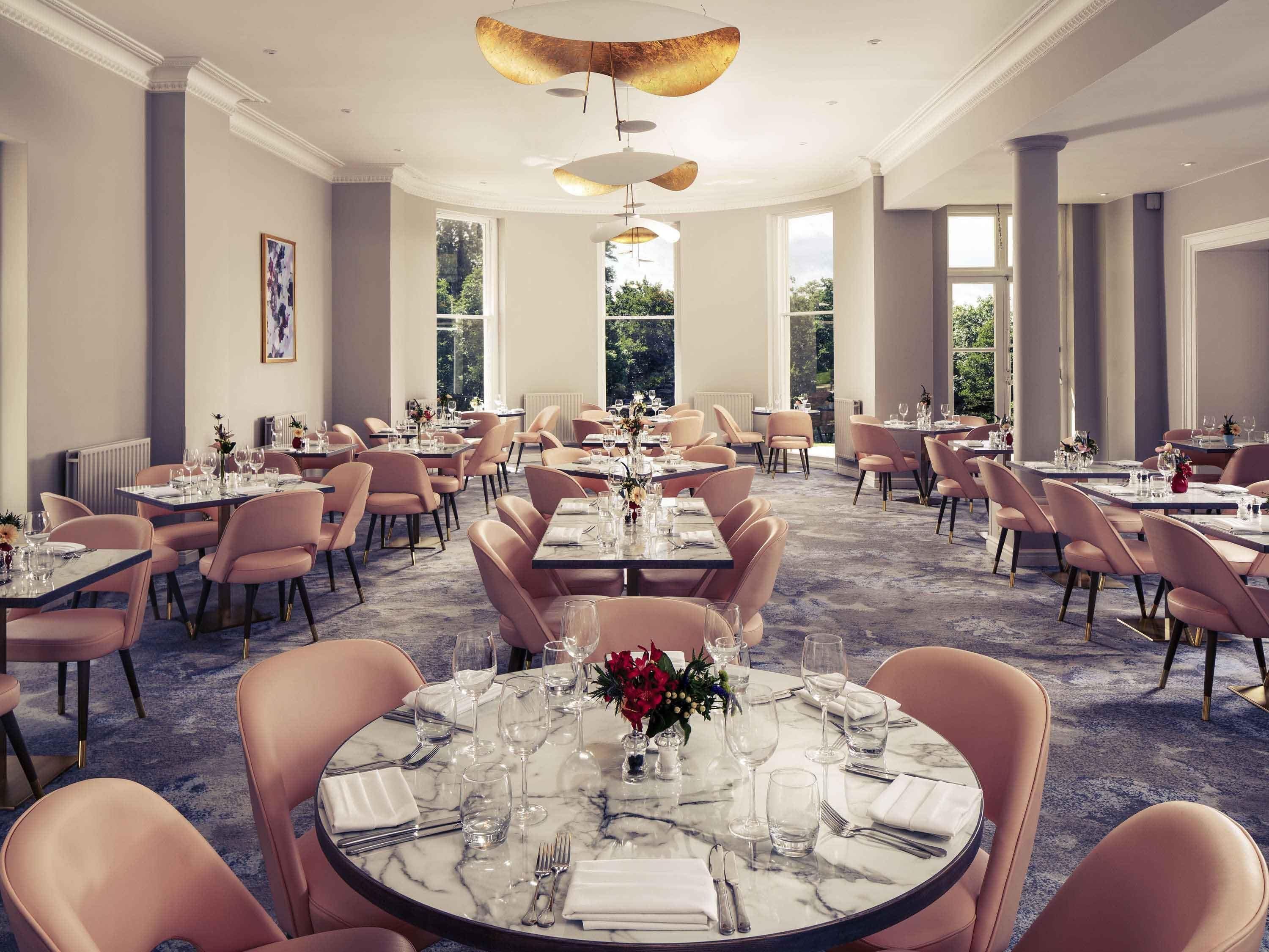 A spacious dining area with round tables and pink chairs, large windows, and a marble floor.