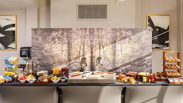 Un bufé de desayuno con diversas opciones de comida, una máquina de café y un amplio telón de fondo con motivos forestales.