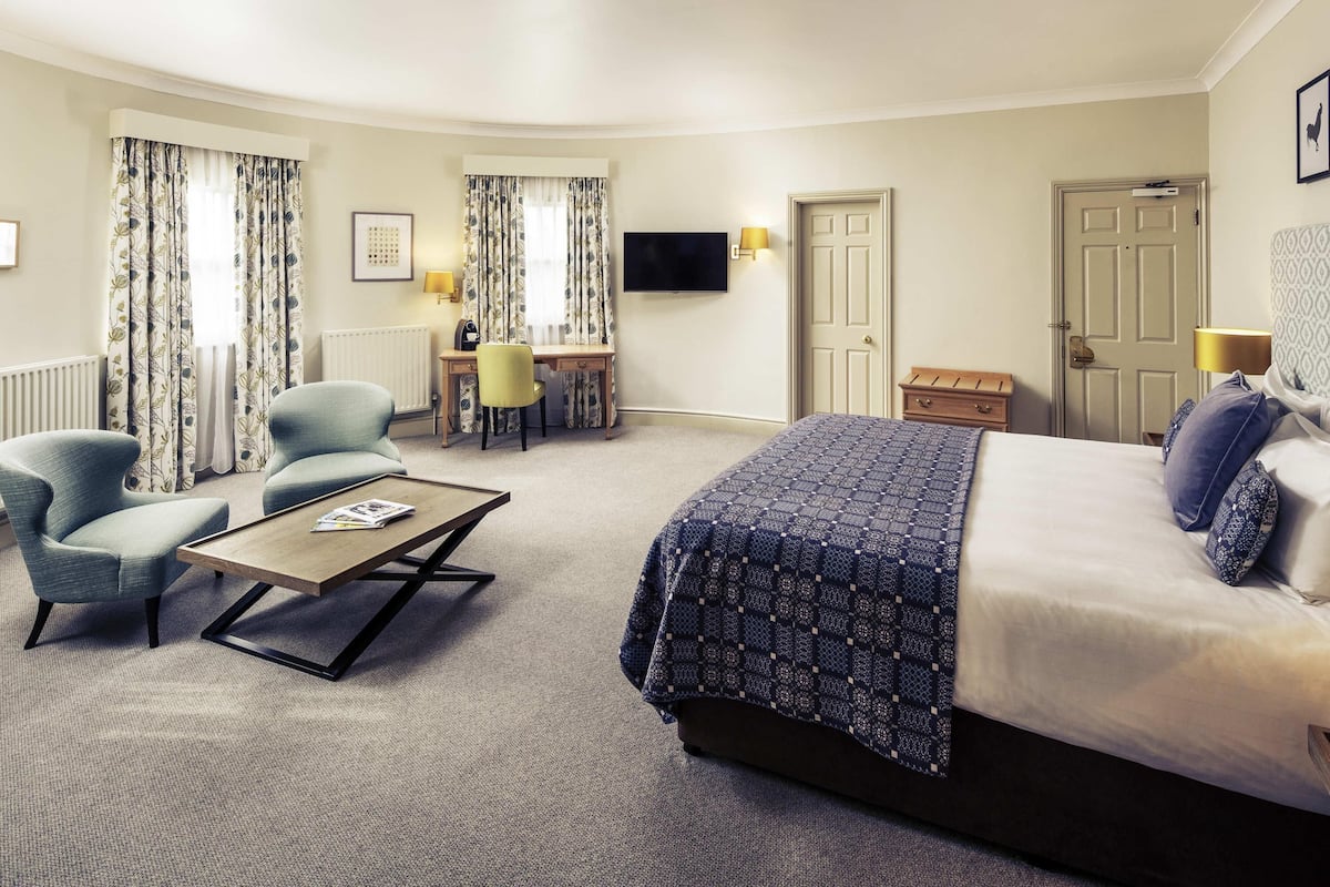 A hotel room with a bed, two armchairs, a desk, a television, and a door.