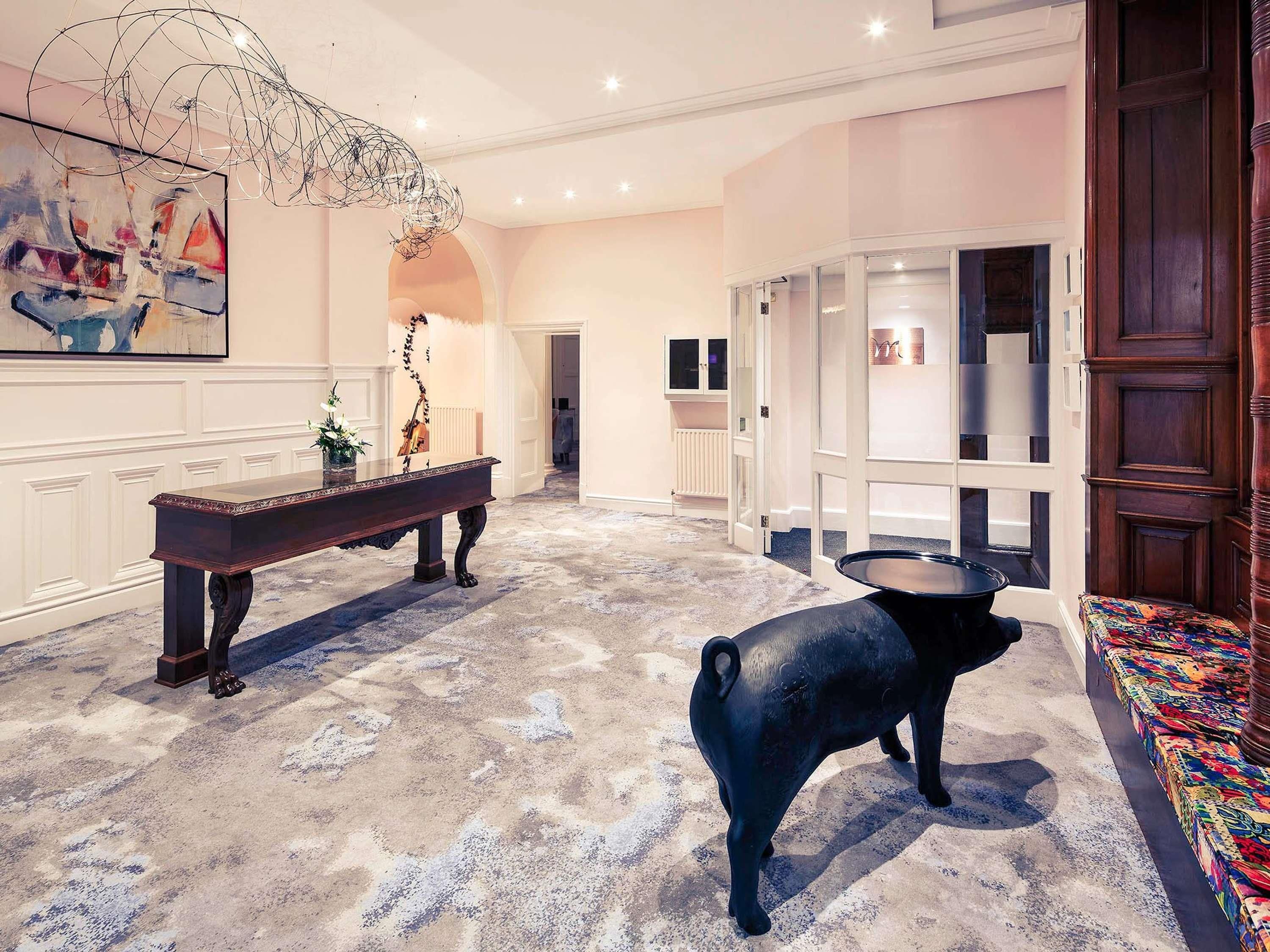 A spacious lobby with a grand piano, a decorative sculpture, and a large black pig statue.