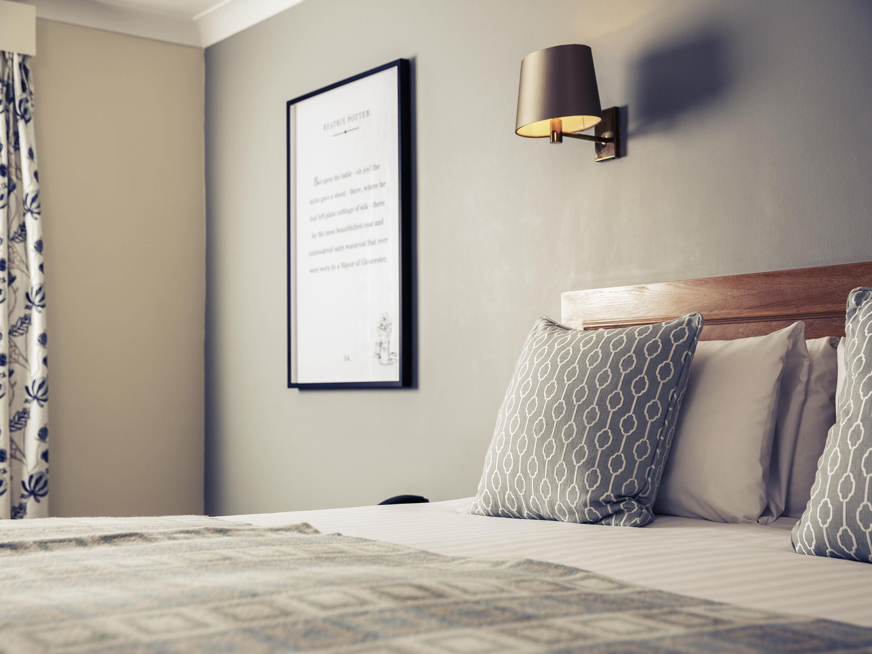 A neatly made bed with patterned pillows, a framed quote on the wall, and a wall-mounted lamp.