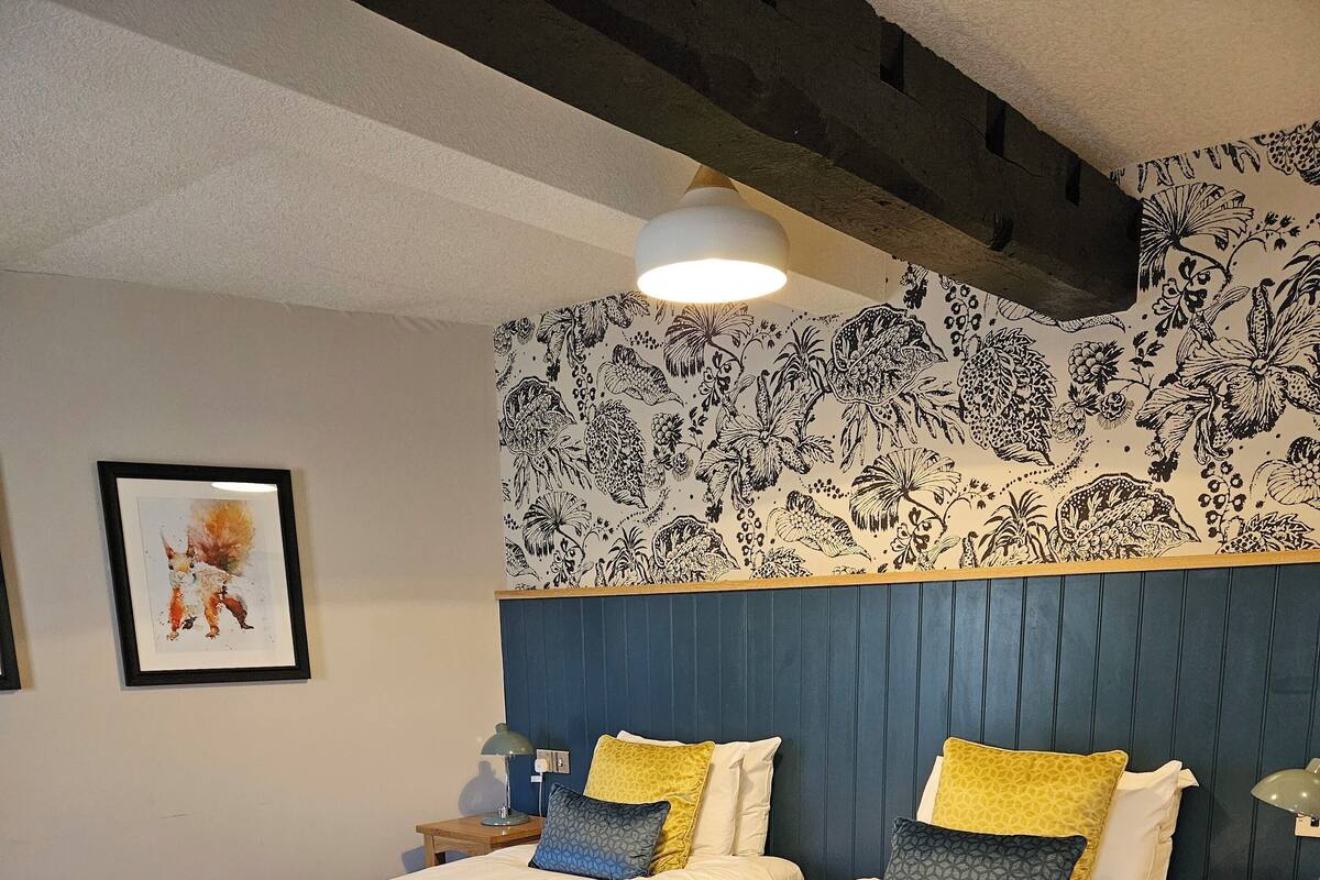 Una cama doble con cabecera, dos mesitas de noche, una lámpara y una pared con estampado floral.