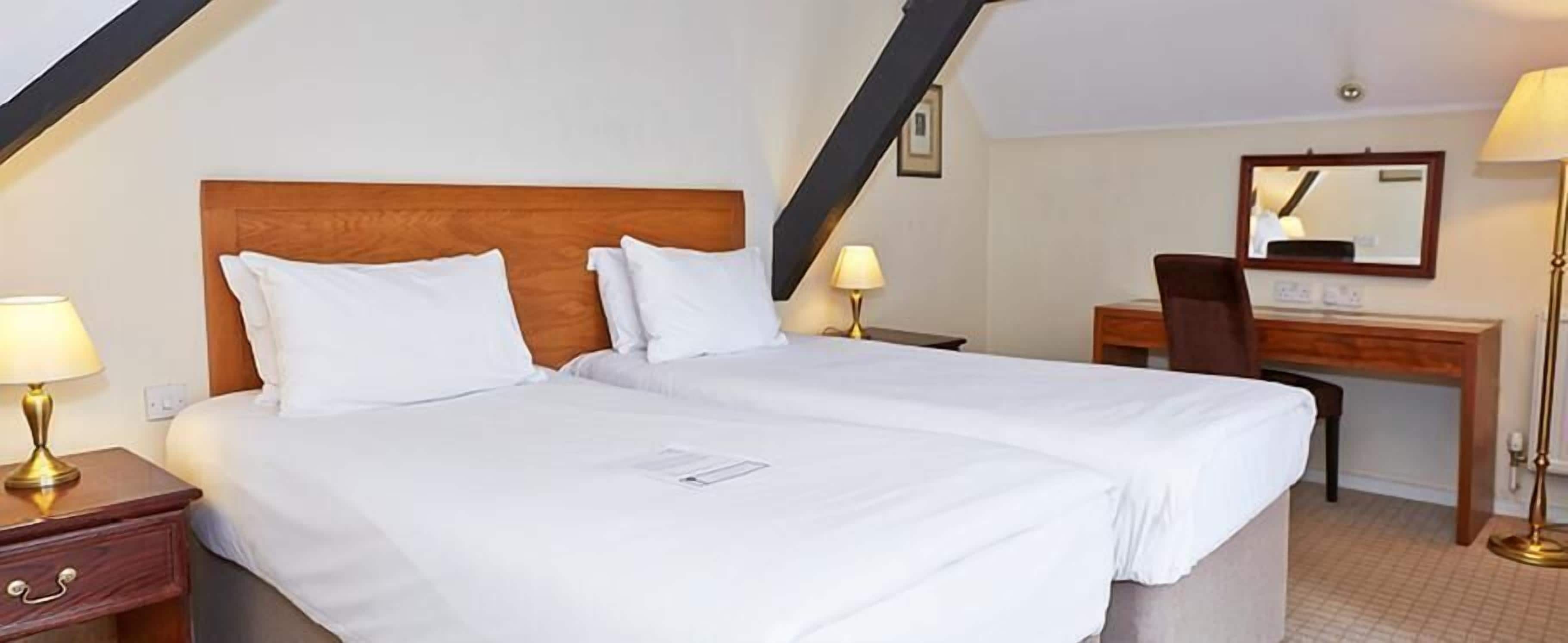 A hotel room with two beds, a desk, and a chair.