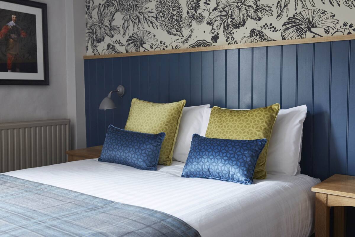 Una cama bien hecha con almohadillas estampadas, un cabecero azul y un diseño de papel tapiz floral.